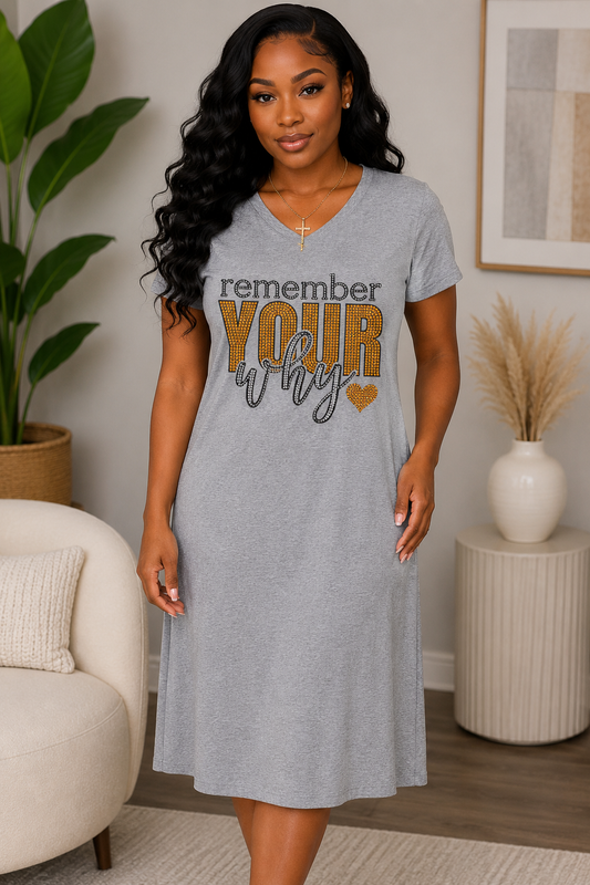 A woman wearing a heather gray V-neck t-shirt dress with the text 'remember YOUR why' printed on the front, standing in a modern living room setting.