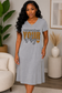 A woman wearing a heather gray V-neck t-shirt dress with the text 'remember YOUR why' printed on the front, standing in a modern living room setting.