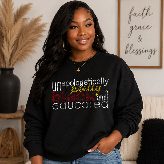 A woman wearing a black crewneck sweatshirt with the text 'Unapologetically pretty black and educated' in white, red, and yellow lettering, posed in a cozy living room setting.